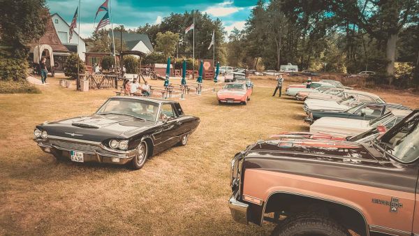 Ein blauer Ford Thunderbird aus den 60ger Jahren fährt auf die Koppel der BigHorn Ranch die im Hintergrund zu sehen ist