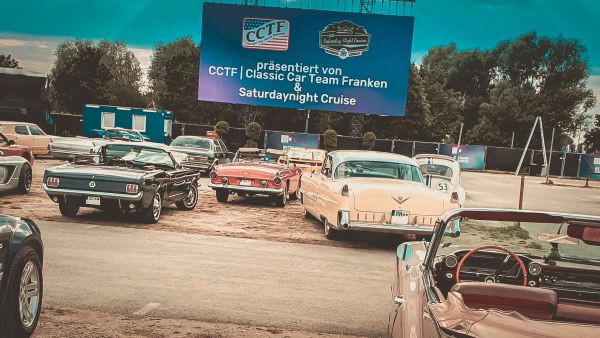 Mehrere US-Oldtimer von hinten mit Blickrichtung auf die riesige LED-Wand des Autokino im Hintergrund