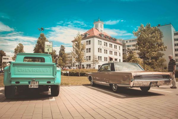Links ein türkis-farbener Pick-Up und rechts ein altes US-Car von hinten. In der Mitte steht zwischen den Oldtimern das Rundfunkmuseum Fürth