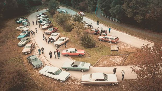 Mehrere klassische US-Car-Oldtimer auf einem Parkplatz aus einer Vogelperspektive von schräg oben