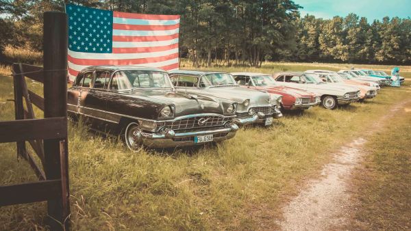 US-Car Oldtimer stehen aufgereiht vor einer riesigen US-Flagge auf der BigHorn Ranch in Birnthon
