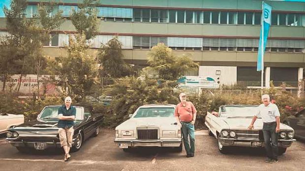 Drei Männer stehen an Ihre klassichen US-Cars angelehnt. Zu sehen unter anderem ein Ford Thunderbird und ein Cadilliac Kabrio