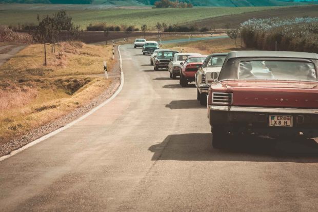 Klassische US-Cars fahren in Kolone vom Fotografen weg in Richtung Horizont