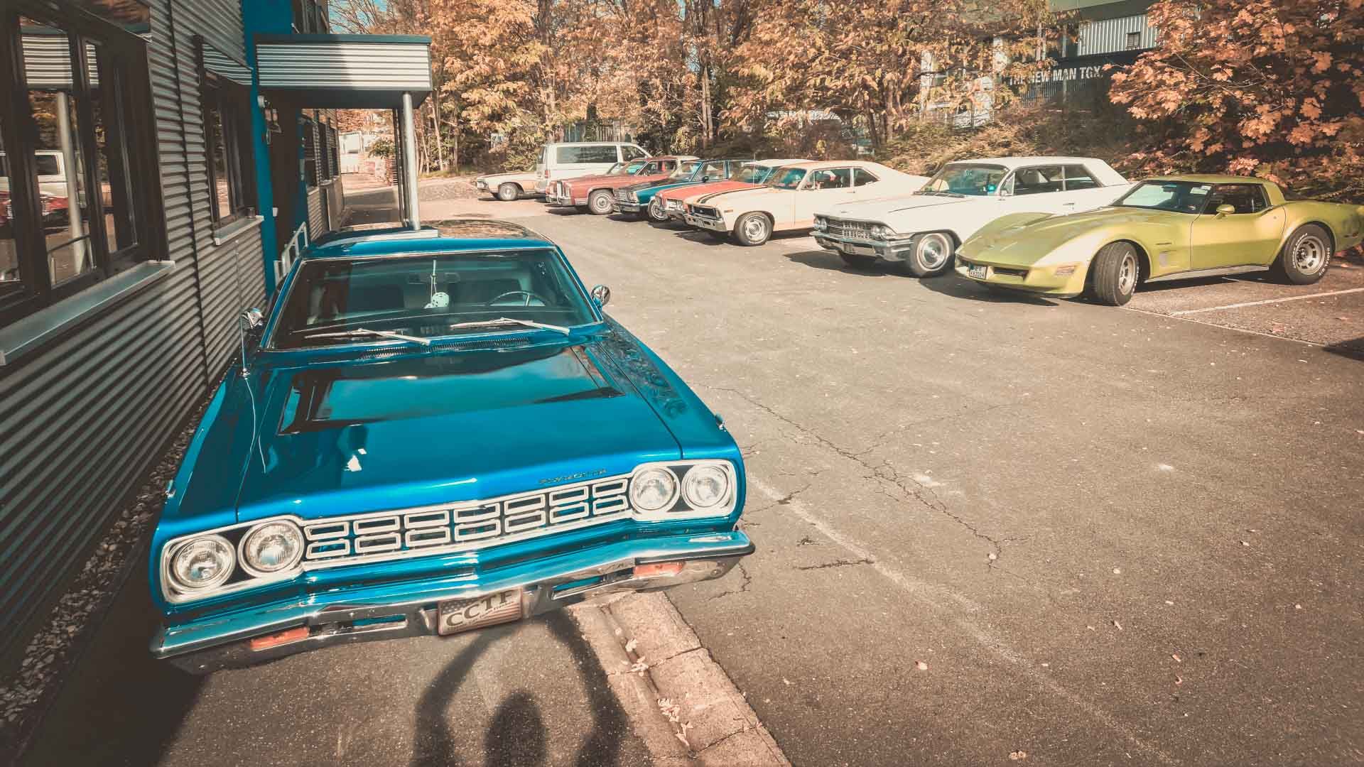 Frontansicht eines blauen Plymouth US-Oldtimer der an einer Hauswand geparkt steht. Im Hintergrund sind weitere geparkte US-Cars zu sehen.